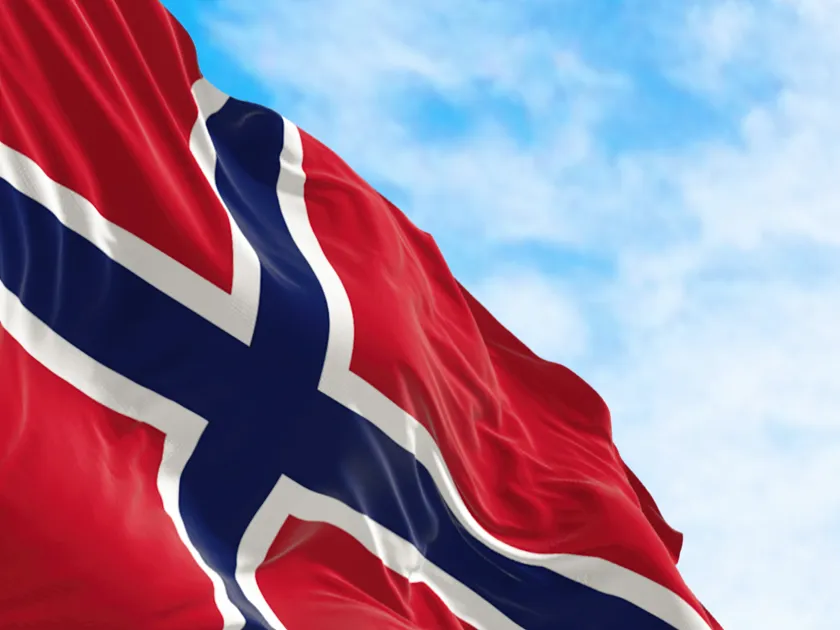 Norwegian flag waving in the wind against a blue sky.