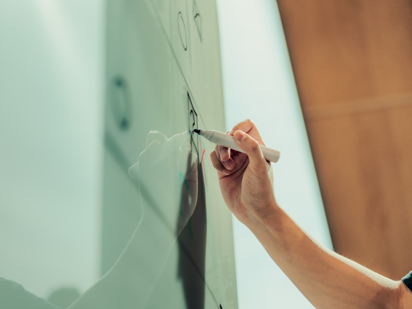 Person skriver med tusj på glasstavle.