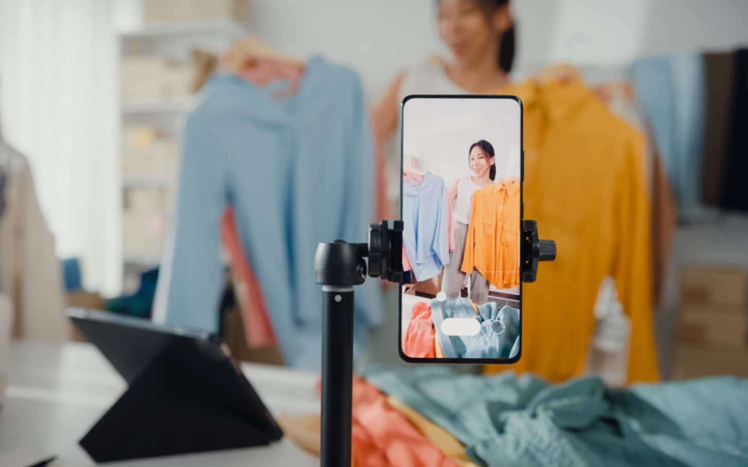 A woman is showing clothes online using a smart phone on a tripod