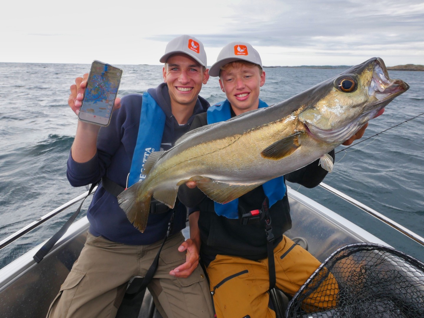 To gutter i en båt med en stor fisk og en mobiltelefon