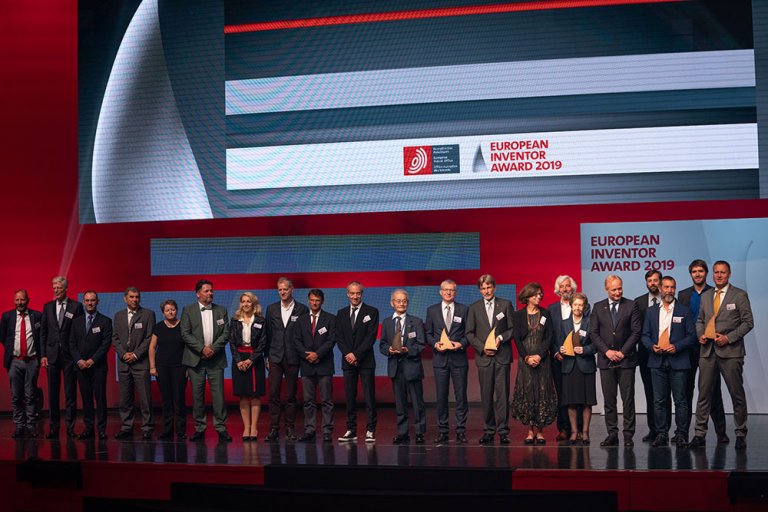 En rekke mennesker på en scene med teksten European Inventor Award bak.