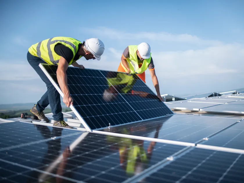 Team of two engineers installing solar panels on roof.