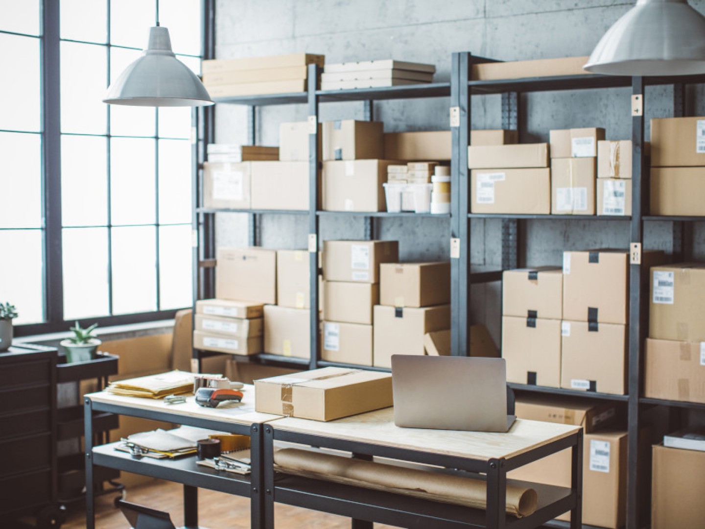 Kontor med laptop, strekkodeskanner og mange pakker i hyller.